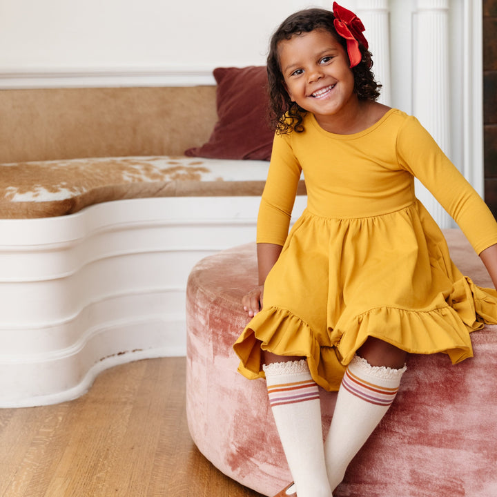 little girl sitting in mustard twirl dress and vanilla striped knee high socks