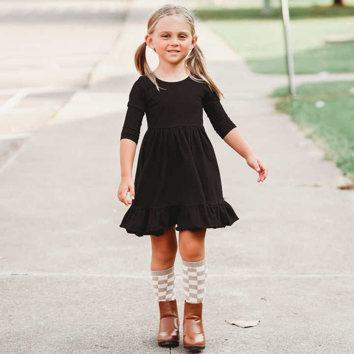 little girls wearing black long sleeve twirl dress and neutral checkered knee high socks