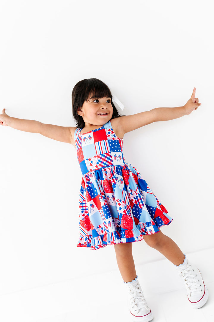 little girl in sleeveless red, white and blue twirl dress with multi pattern fourth of July inspired patchwork print and lettuce trim midi socks