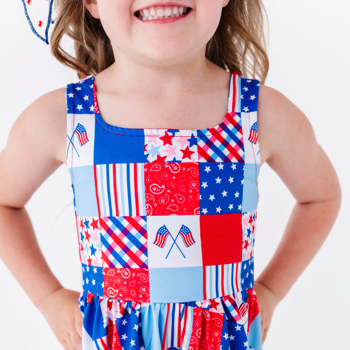 young girl in patchwork print sleeveless twirl dress with red, white and blue gingham, paisley, stripe, star and flag print for fourth of July