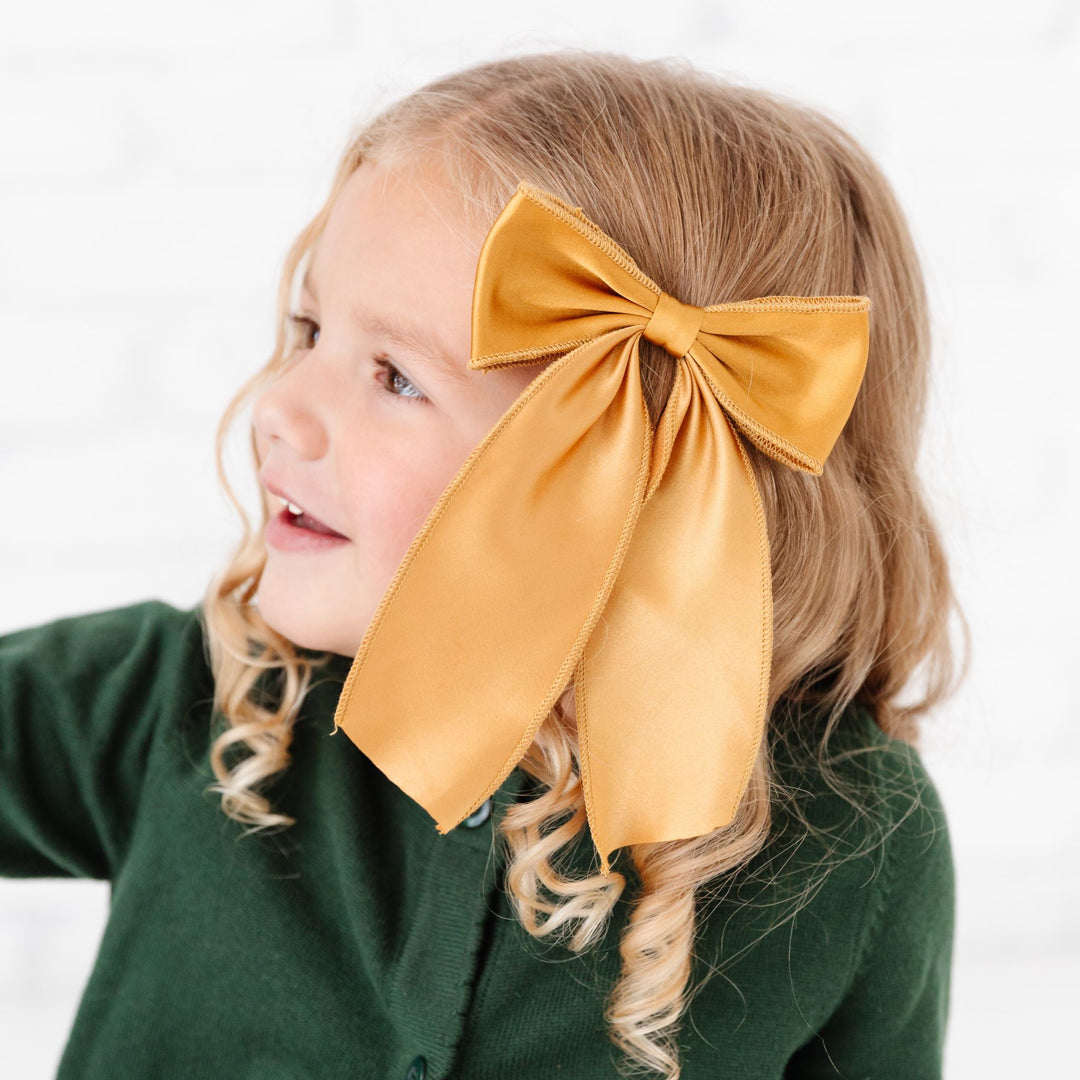 little girl in solid gold satin Christmas bow and forest green knit cardigan