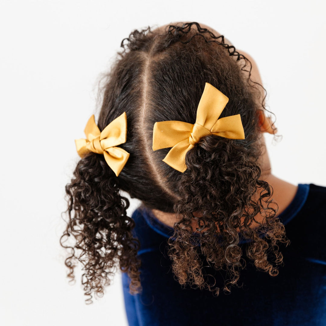 little girl in deep blue winter velvet twirl dress and gold satin pigtail bows on clips