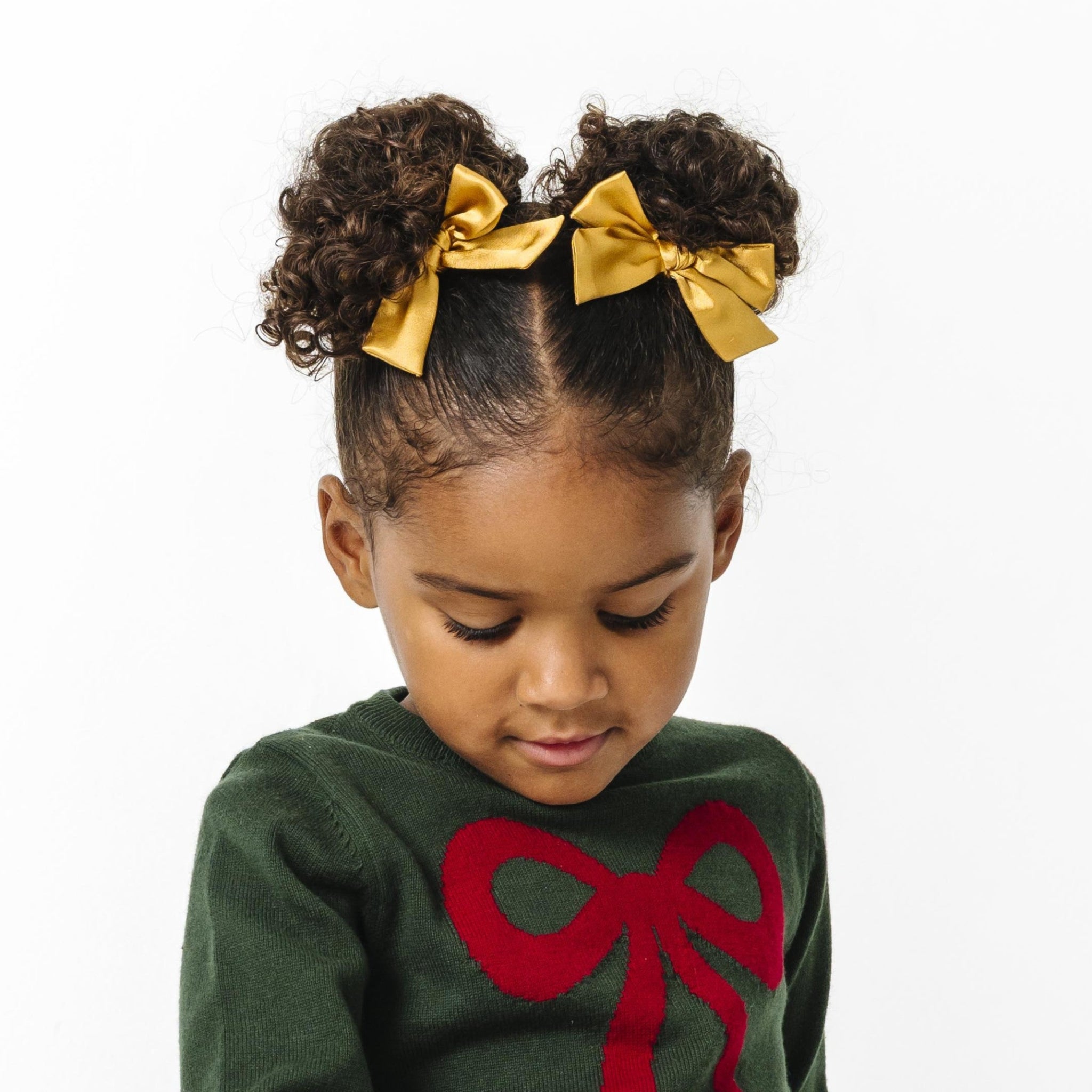 little girl in gold satin pigtail bows on clips paired with forest green and crimson red Christmas bow sweater
