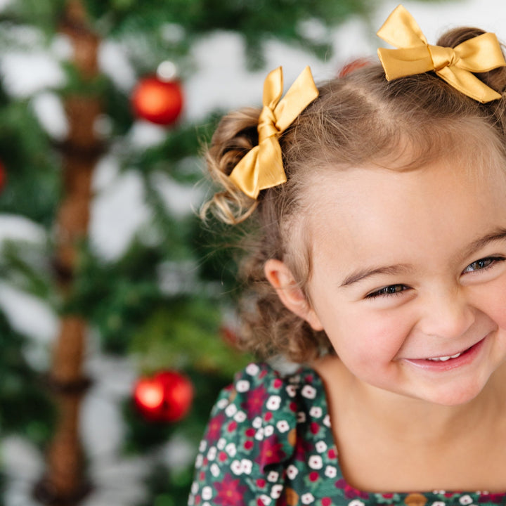 little girl in poinsettia print dress with matching gold satin pigtail bows