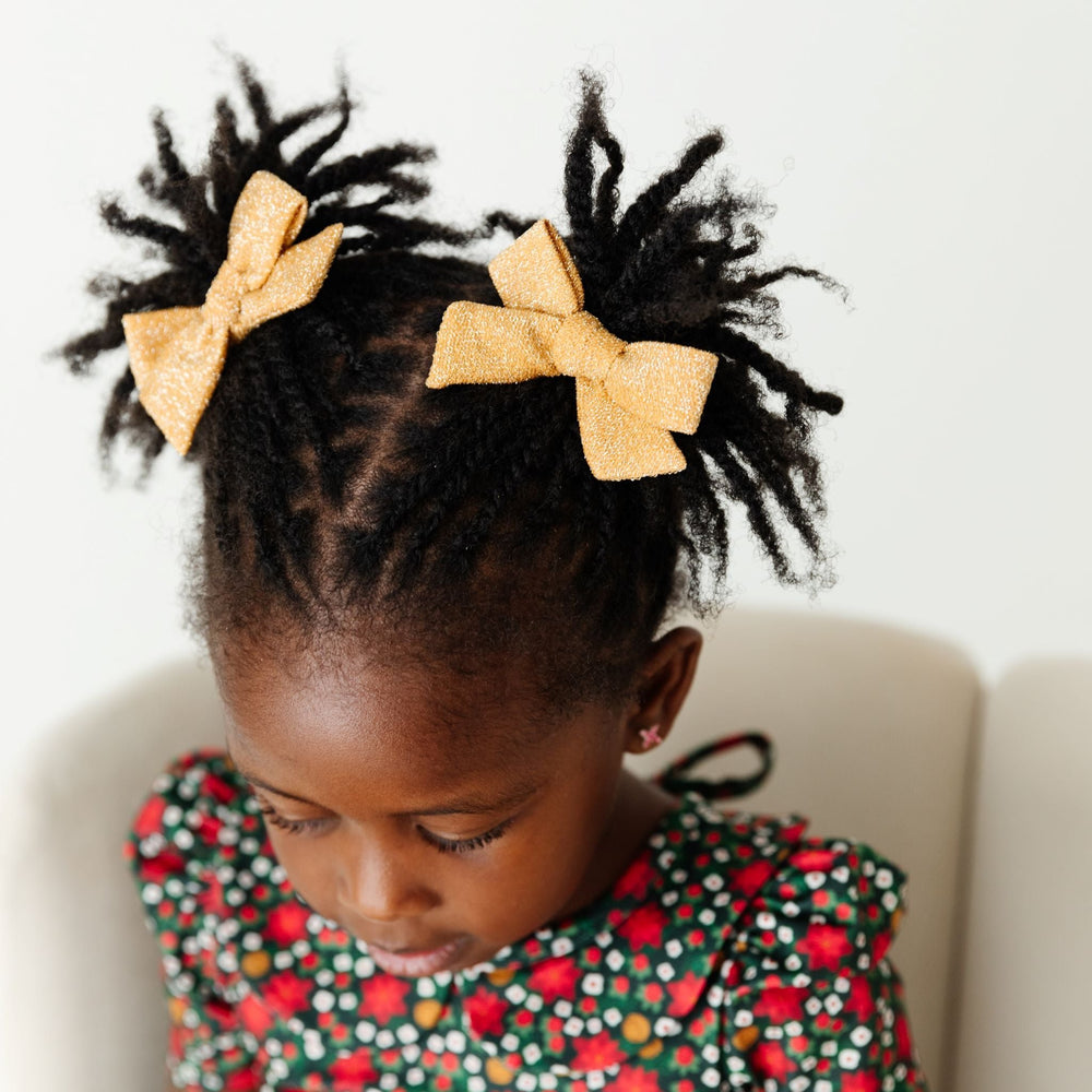 Little girl in sparkly gold pigtail bows to match poinsettia Christmas outfit