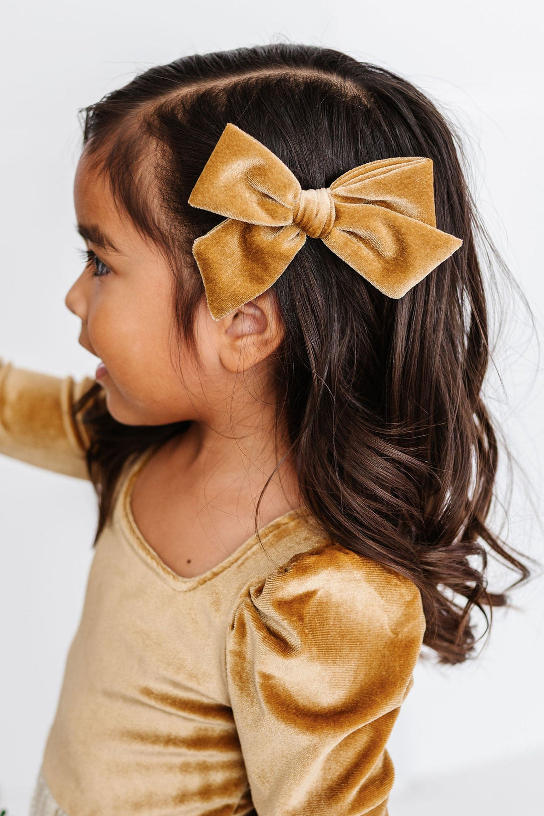 girl wearing gold velvet hair bow with matching gold velvet dress