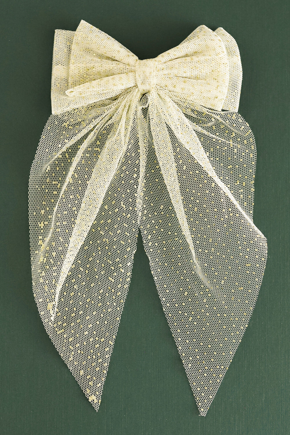 A decorative hair bow made from sheer champagne-colored organza fabric with small gold dot embellishments, set against a dark green background.