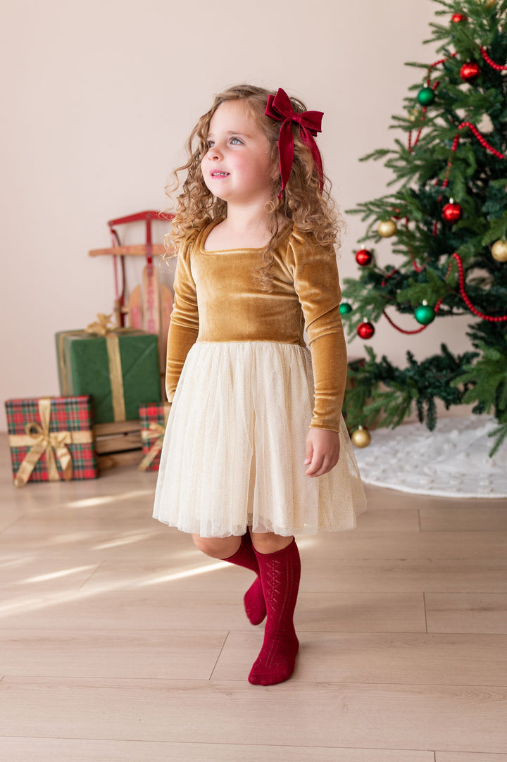 girl wearing gold fancy christmas dress with crimson red hair bow and matching crimson red pointelle knee high socks