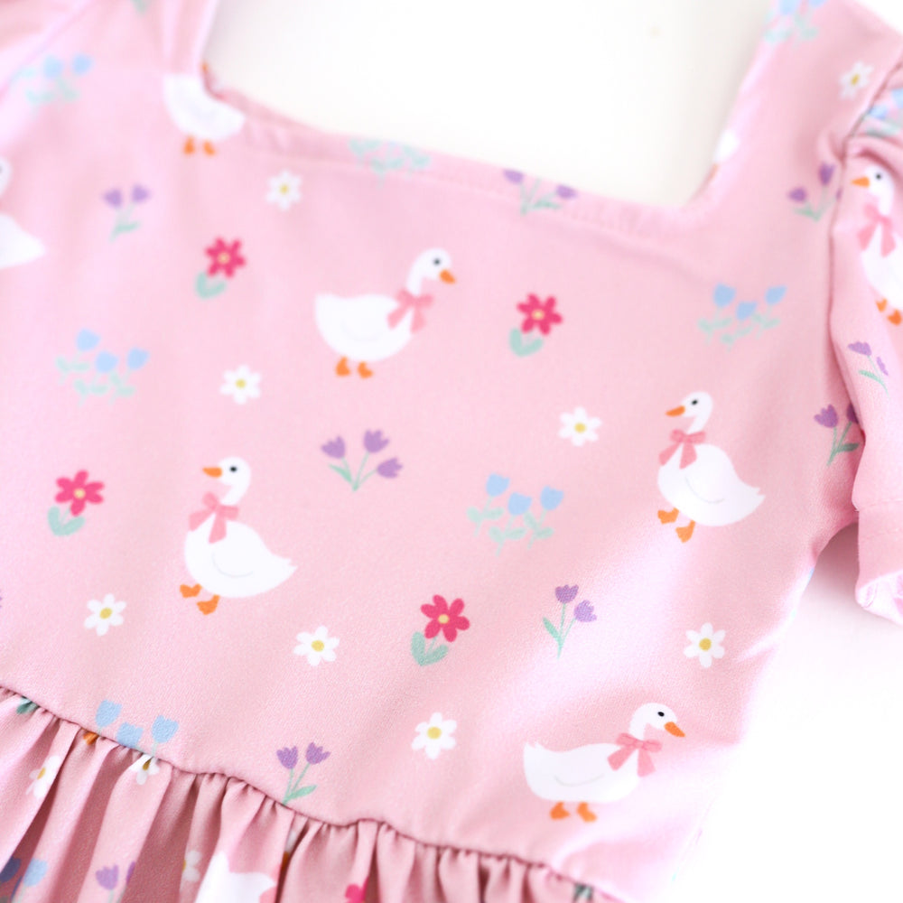 closeup of pastel pink twirl dress bodice featuring little white geese wearing pink bows and petite flowers in various spring shades