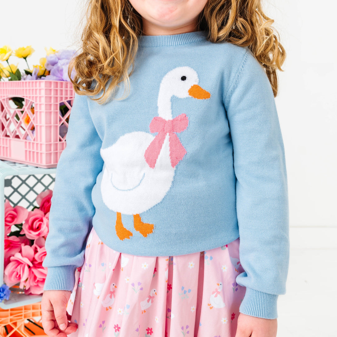 close-up of little girl in pastel blue sweater with white goose design and matching pink goose dress for Easter