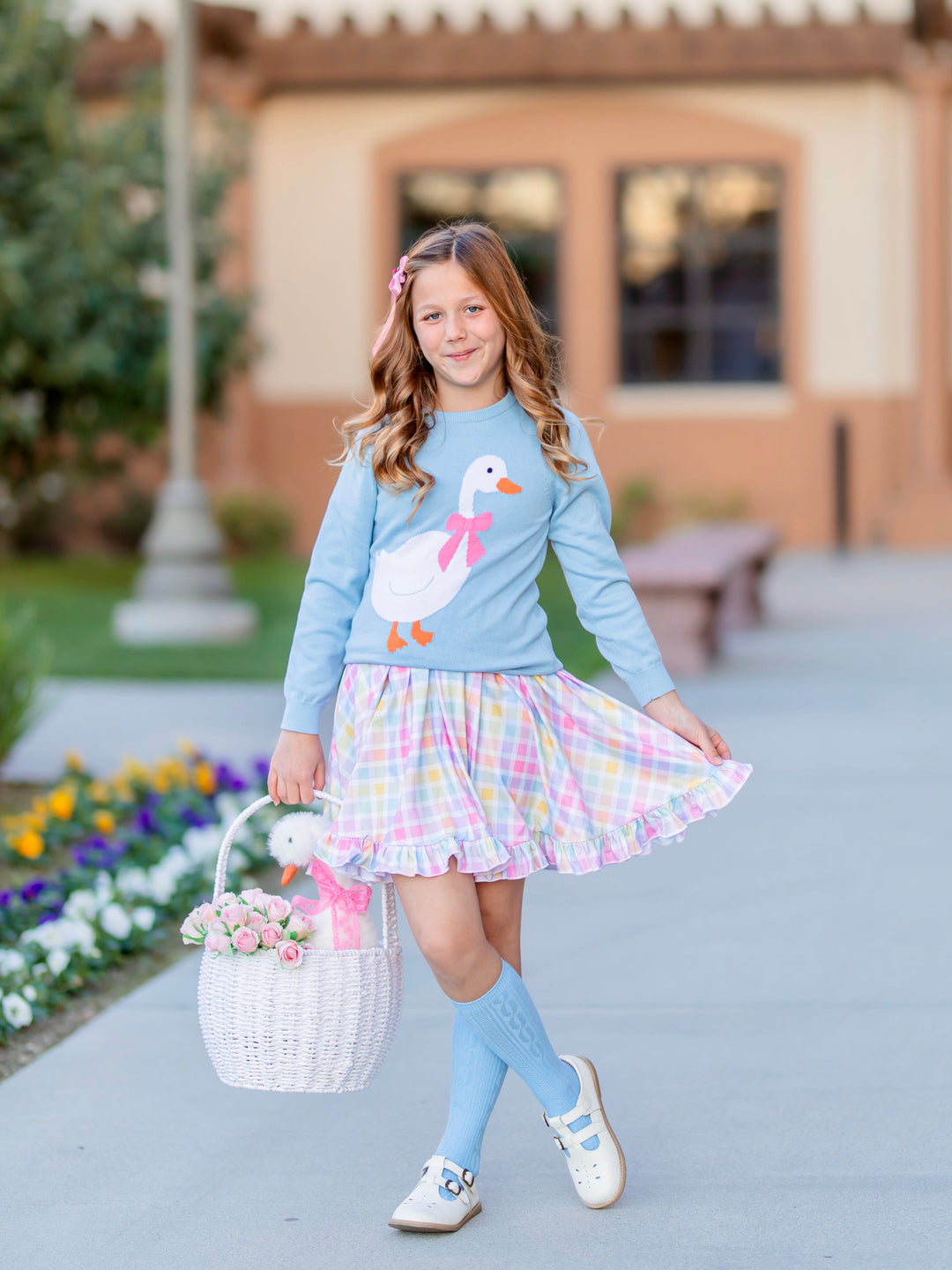 girl holding Eater basket with flowers and toy goose wearing light blue knit sweater with white goose design paired with matching blue cable knit knee highs and spring gingham twirl dress