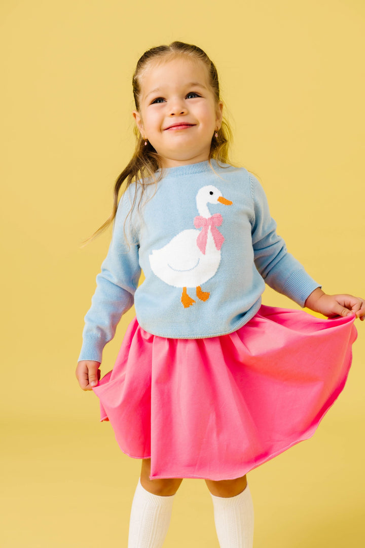 little girl in pastel blue sweater with white goose design and pink bow paired with matching pink skort and white knee highs