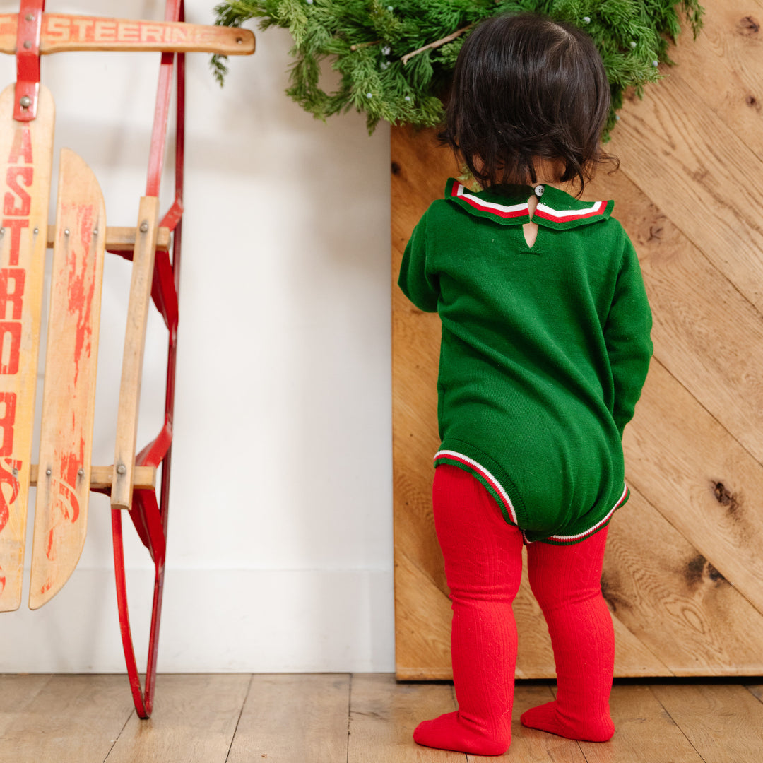 back detail of little girls green christmas sweater romper. paired with bright red christmas tights