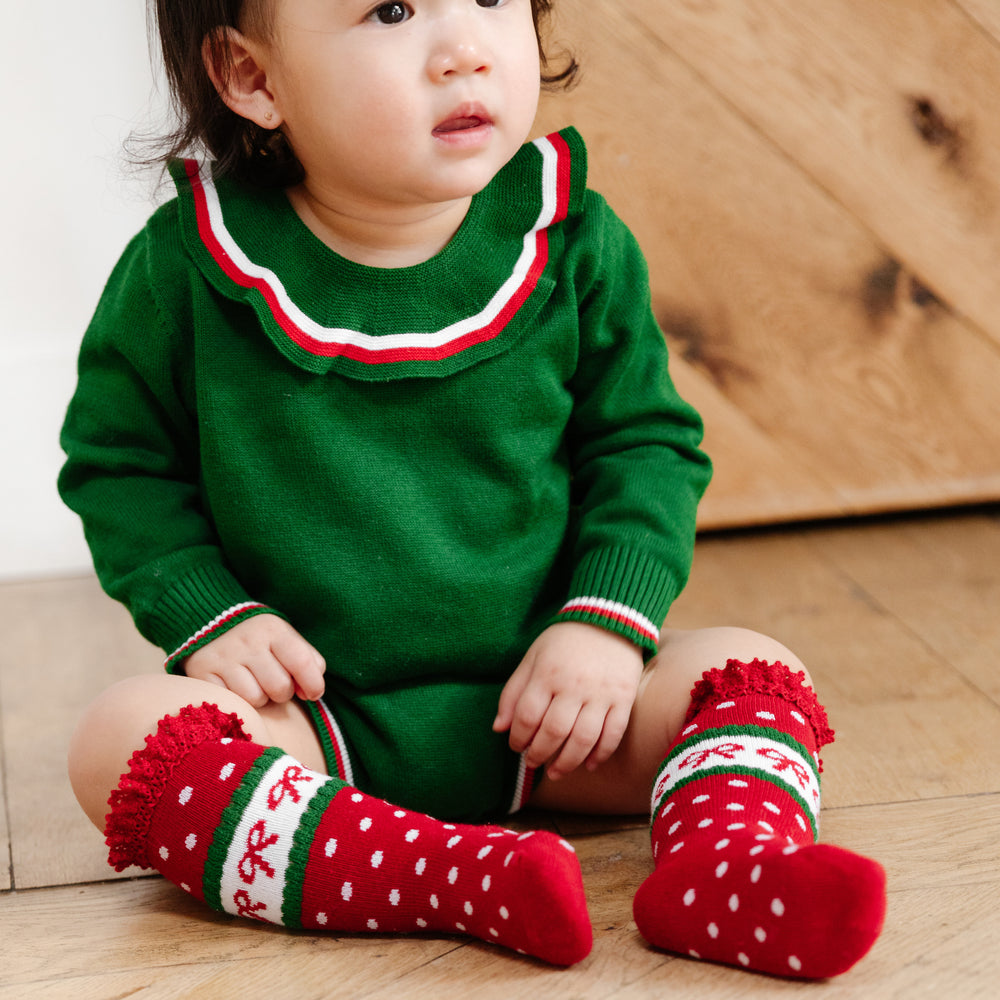 little girl sitting on floor wearing christmas sweater romper in green with red bow christmas socks