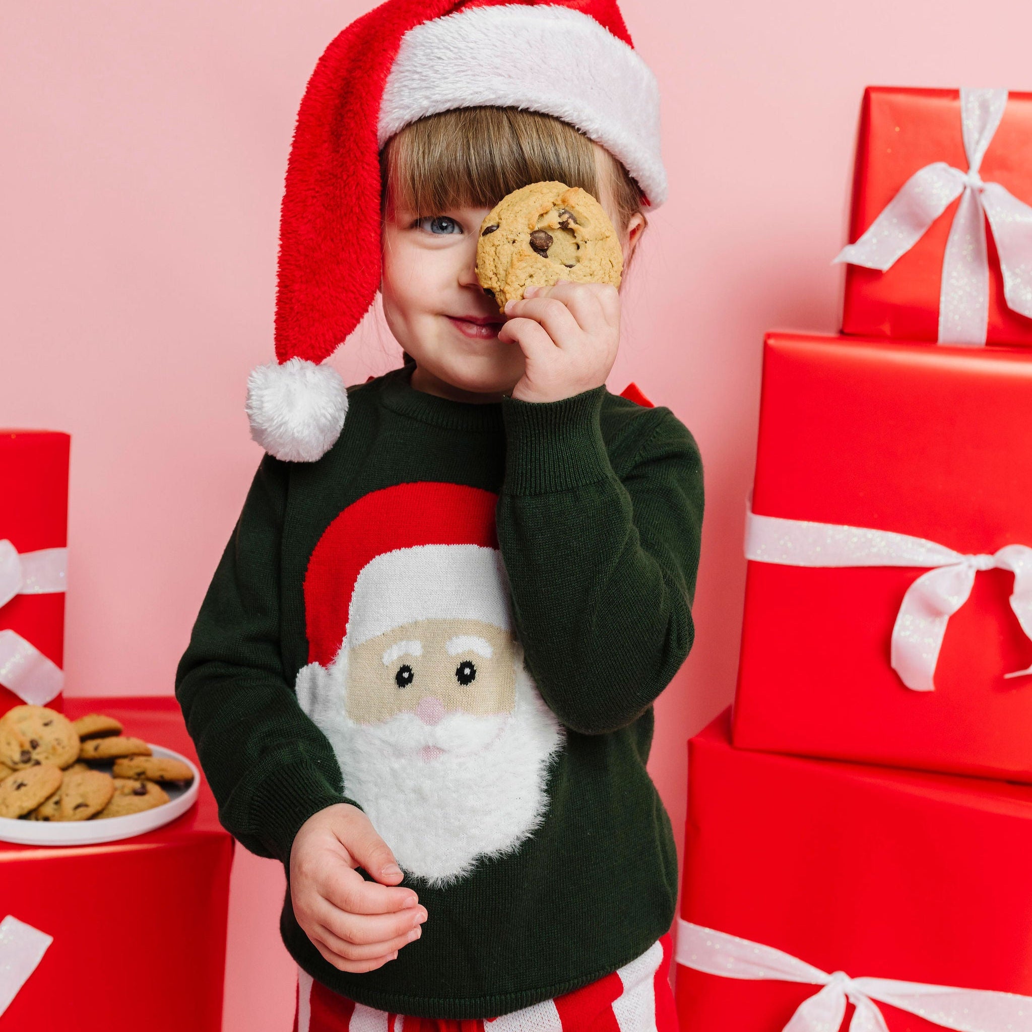 child wearing Santa hat and holding cookie in forest green pullover sweater with fluffy Santa design