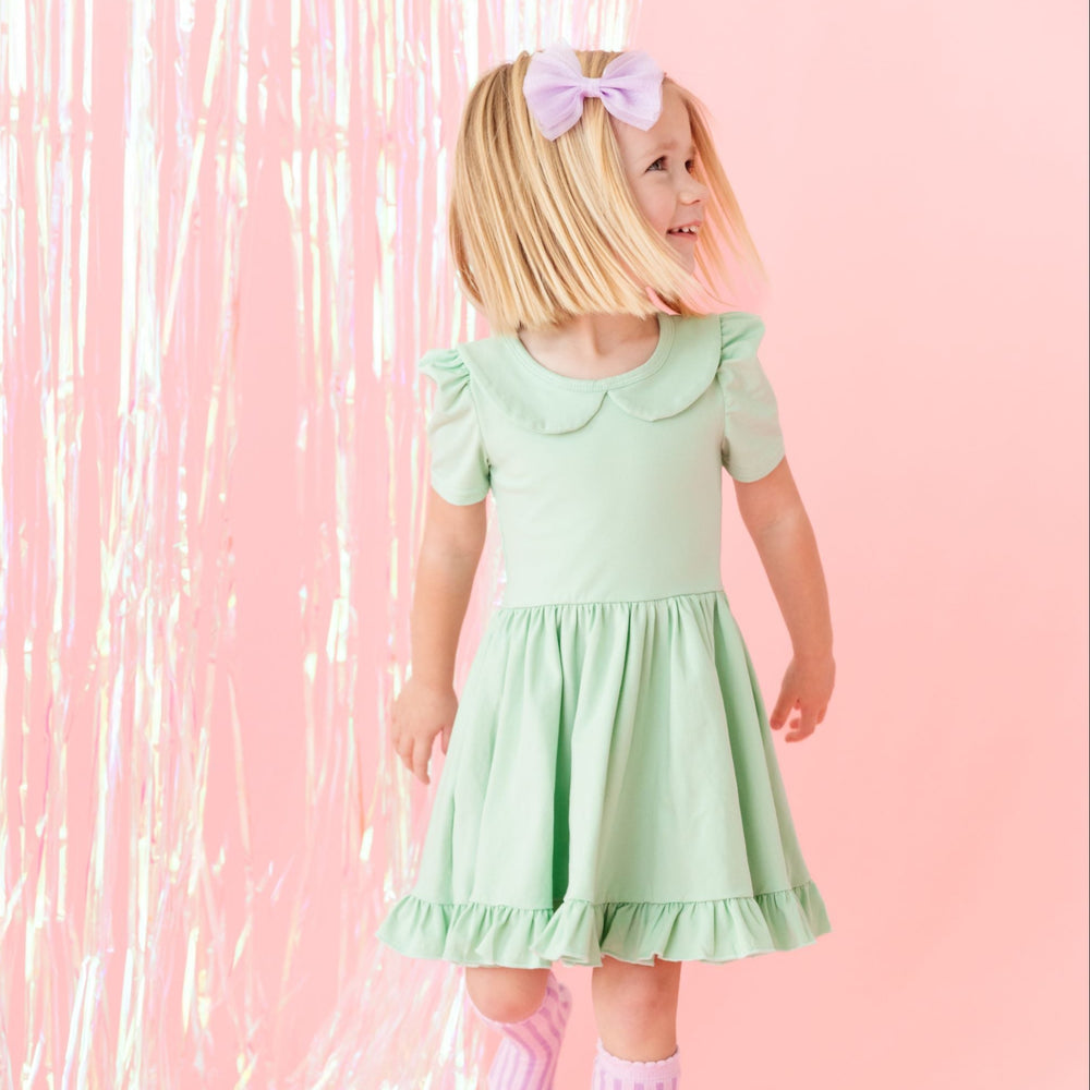 little girl in pastel green twirl dress with lavender knee-highs and bow 