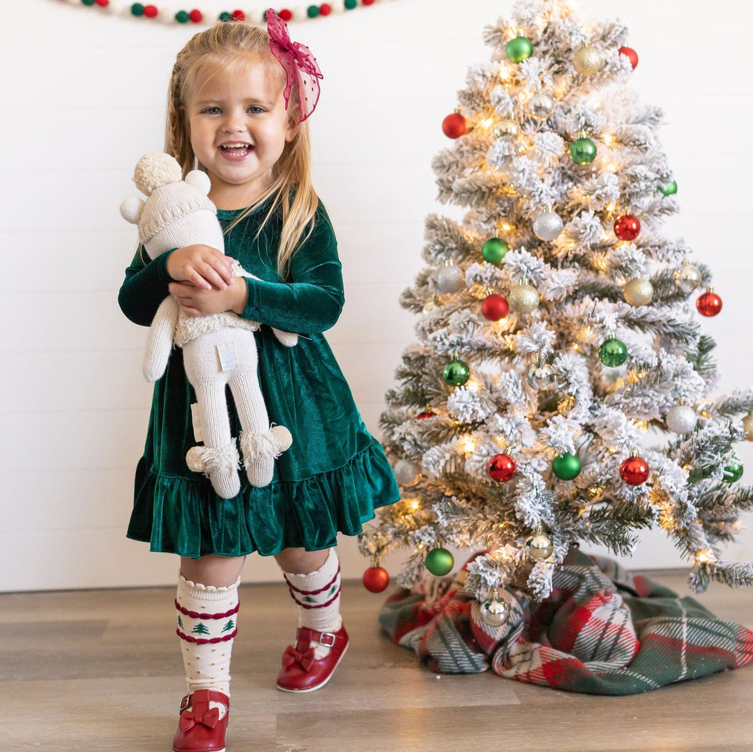 little girl in front of christmas tree wearing green velvet dress and tree knee highs 