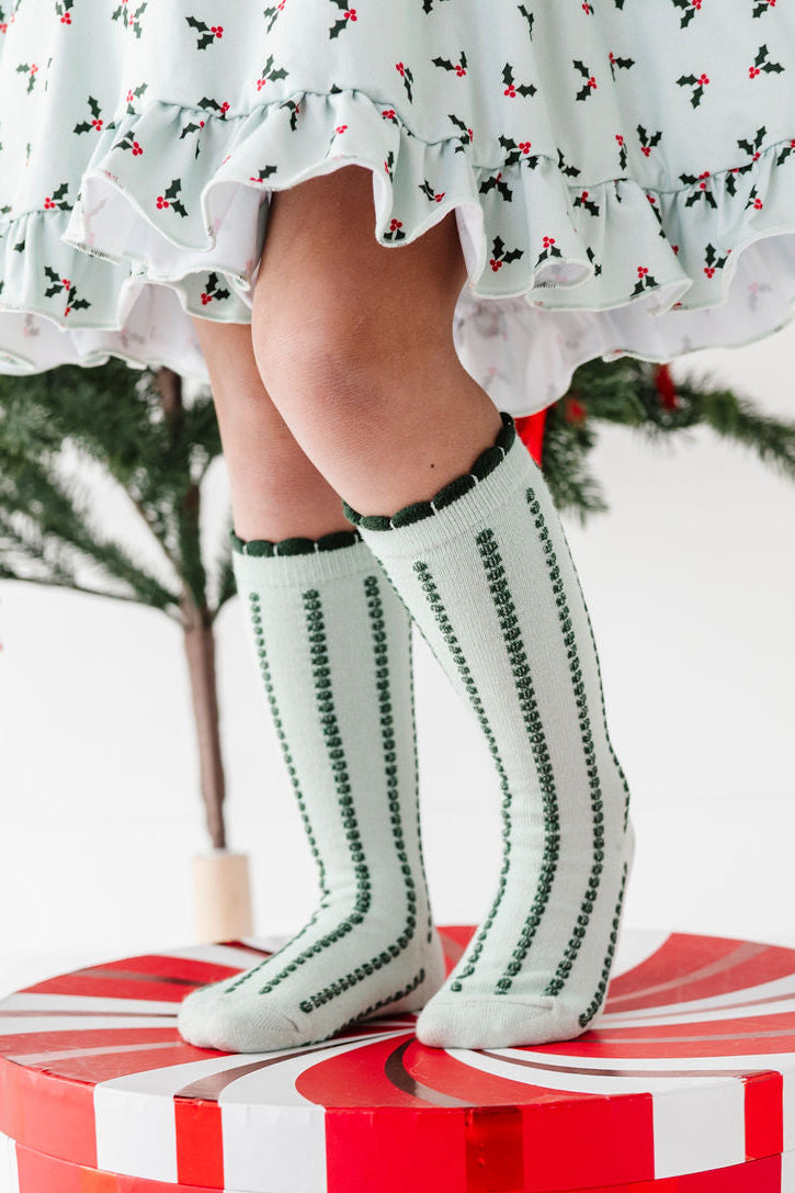girl wearing mint green knee high socks with forest green vertical stripes and matching christmas holly dress