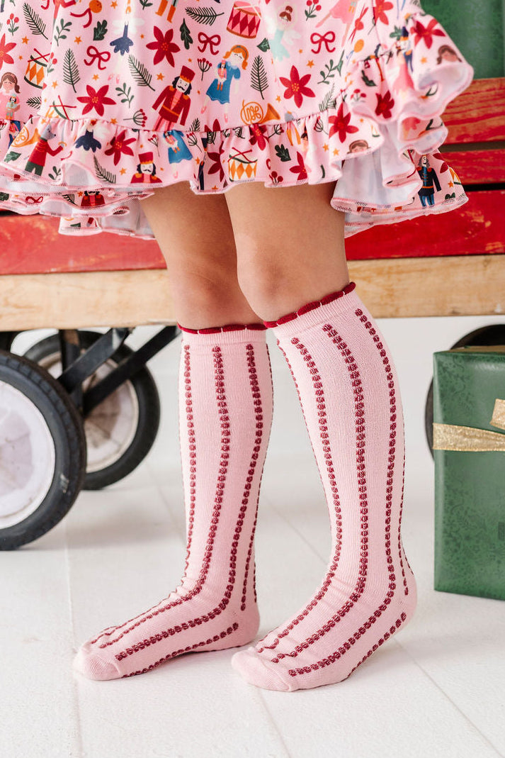 little girl wearing pink and red striped knee high socks with matching Nutcracker themed dress for Christmas