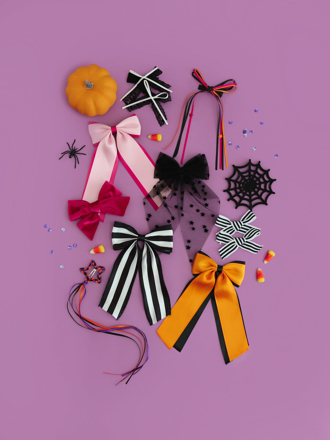 assortment of Halloween hair bows on clips in shades of pink, orange and black photographed on purple background with confetti and candy corn