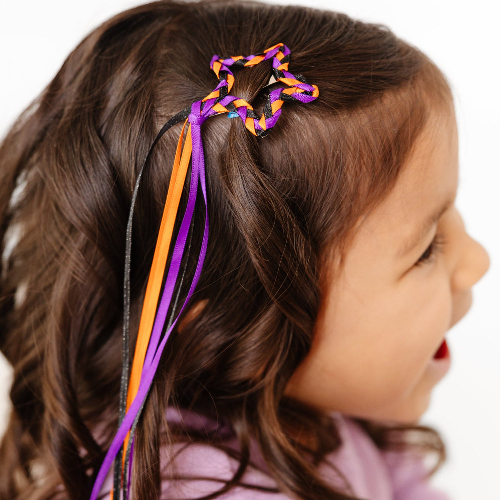 little girl in hair clip with black, orange and purple ribbon streamers braided into star shape for Halloween outfits