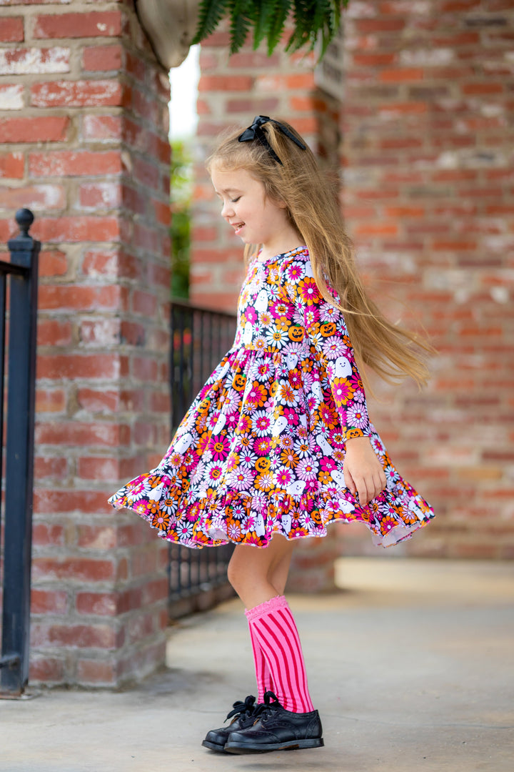 little girl twirling in long sleeve velvet twirl dress with Halloween floral print in shades of black, white, pink and orange paired with two-tone, pink striped knee high socks