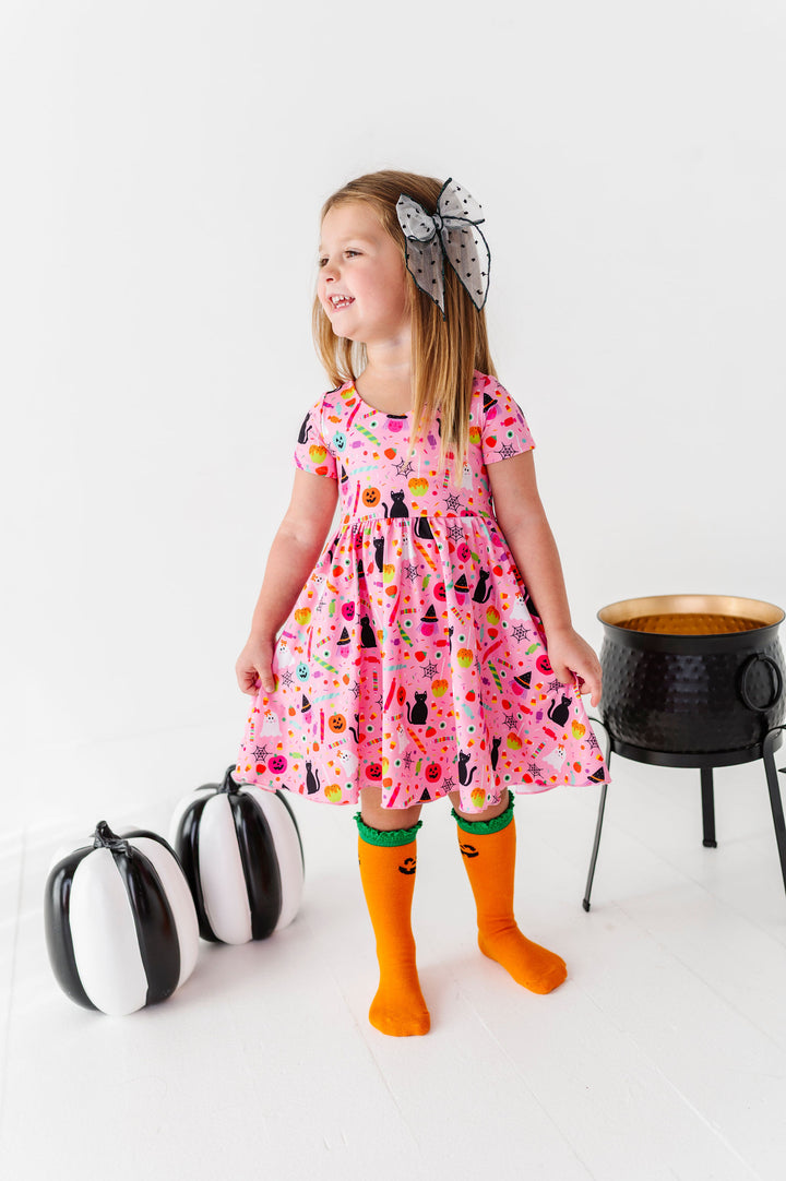 little girl wearing pink halloween print dress with jack-o-lantern knee high socks