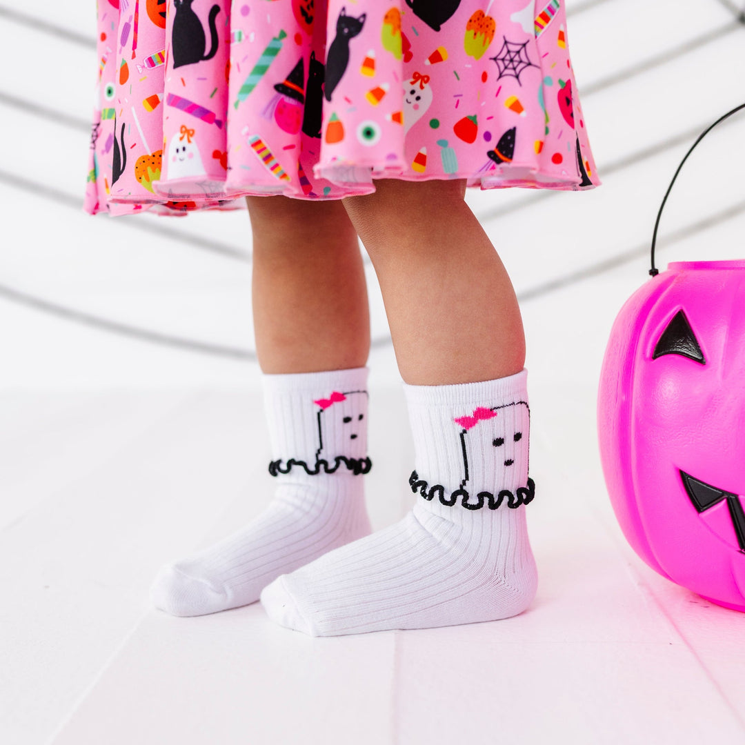little girl with pink pumpkin bucket in white ribbed midi socks with ghost design and ruffled detail at the ankle paired with pink Halloween print party dress