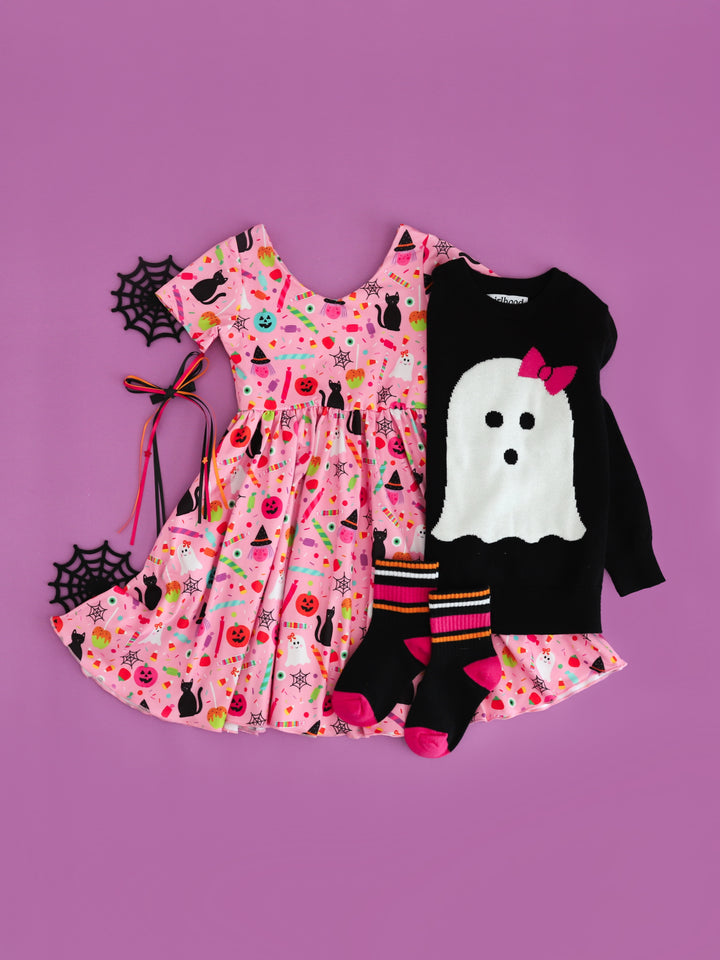 girls pink v-neck twirl dress with black cat, pumpkin, ghost and candy print paired with black sweater featuring ghost design and matching midi socks and hair bow