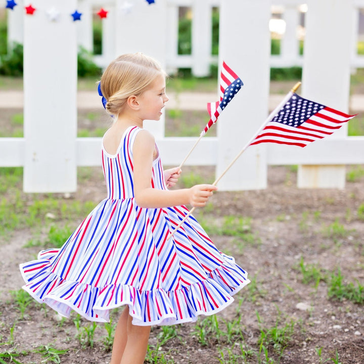 little girl twirling in 4th of july striped dress holding an american flag in each hand