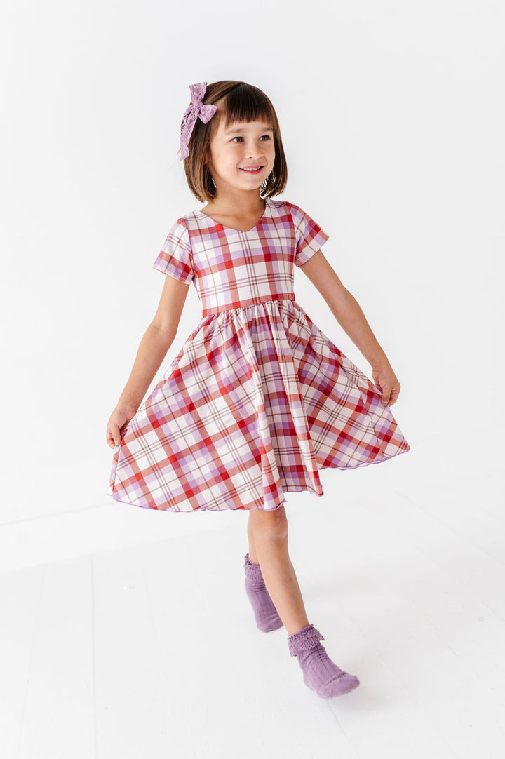 girl wearing purple and rust plaid dress with matching purple socks and hair bow