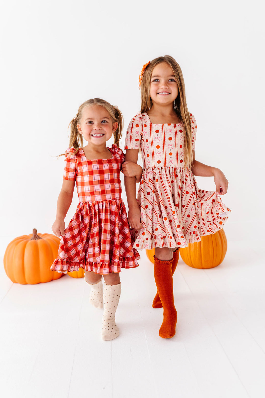 two girls wearing pink and orange harvest themed dresses with matching knee high socks