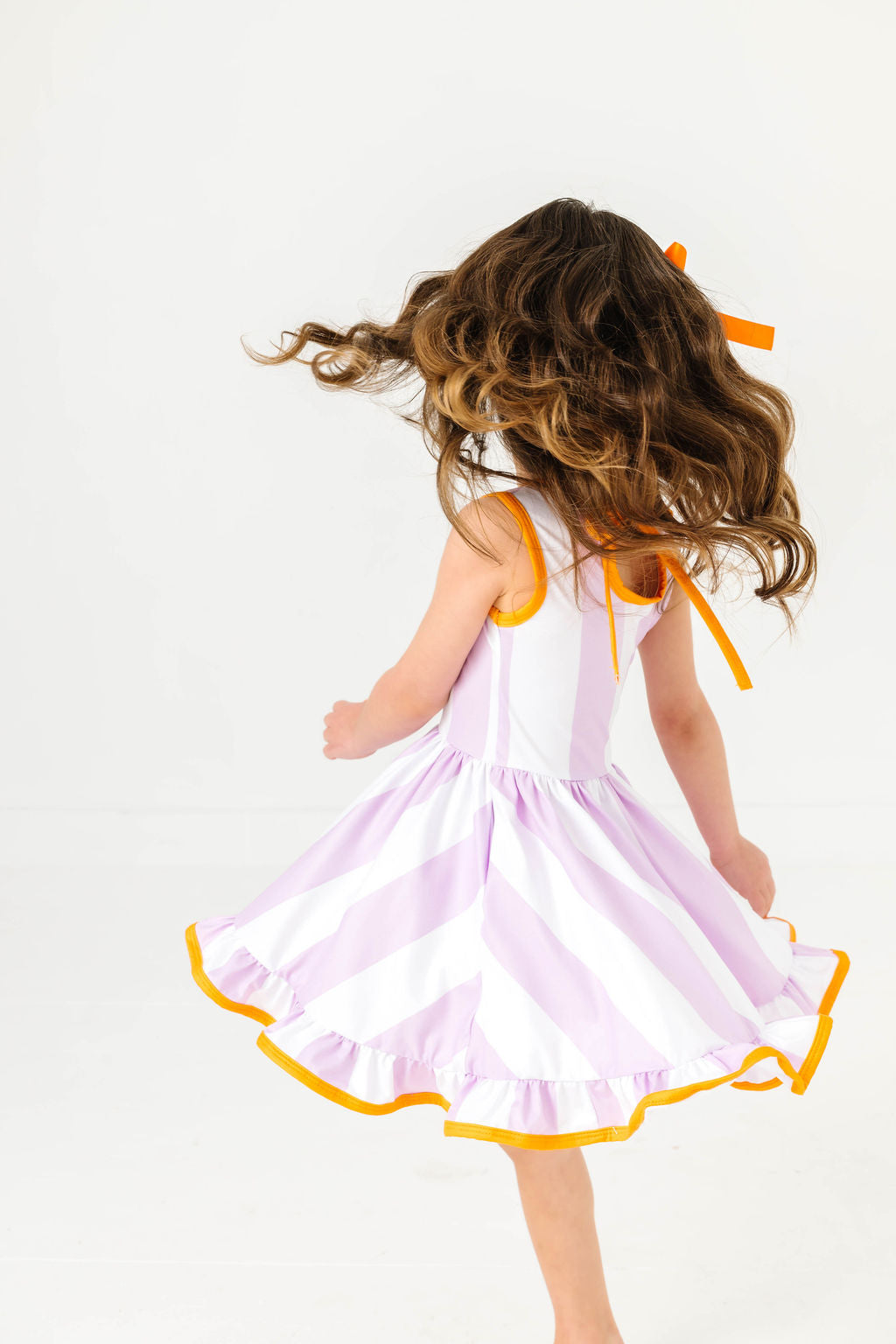 girl twirling in purple and white wide striped summer twirl dress with orange binding