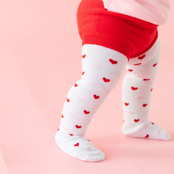 closeup of baby in pink and red heart pattern tights paired with bright red sweater bloomers