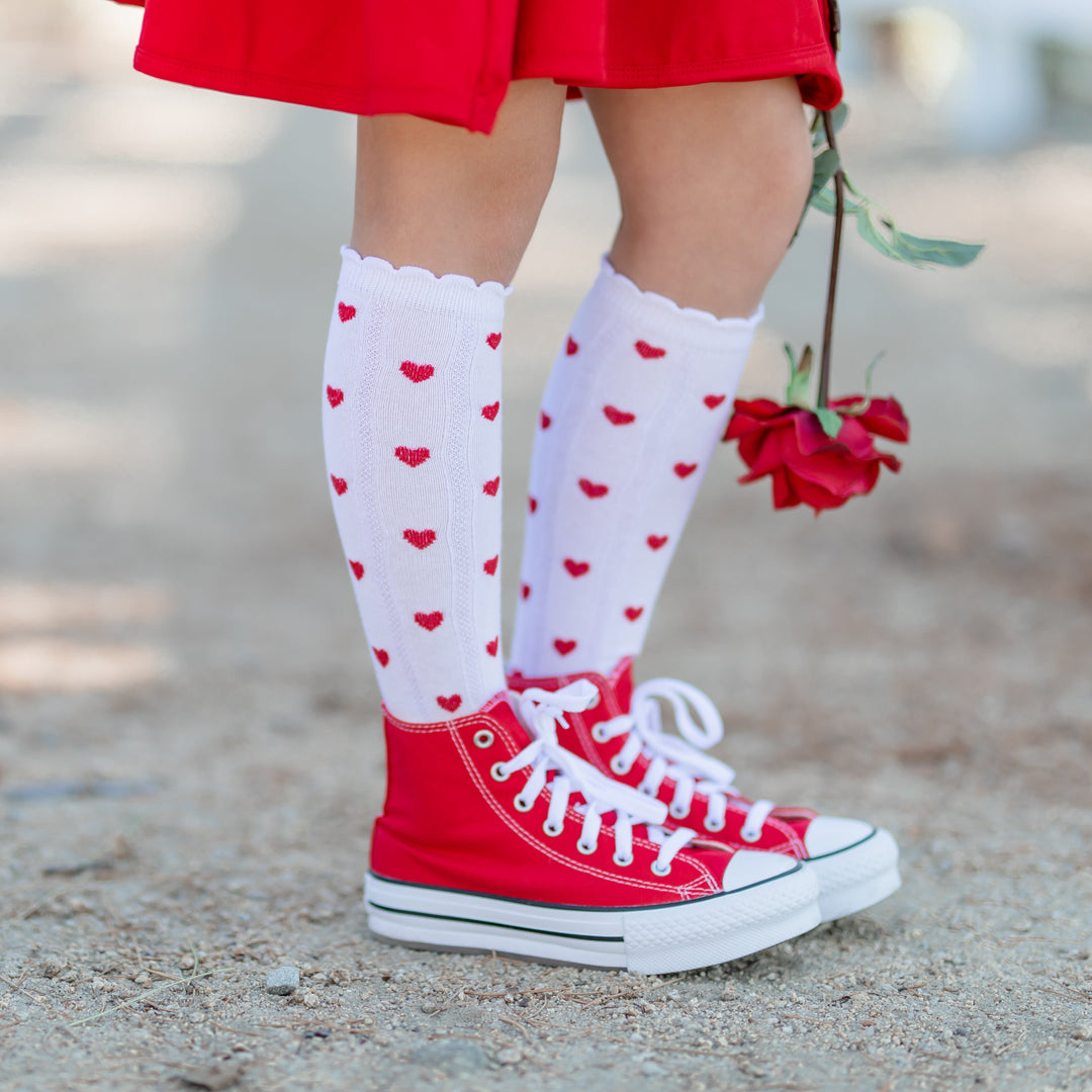 closeup of girl in white scallop trimmed knee high socks with red heart pattern paired with red cotton dress and red sneakers