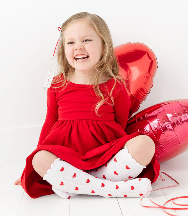 little girl holding valentine's balloons wearing red long sleeve cotton dress and white knee high socks with red hearts