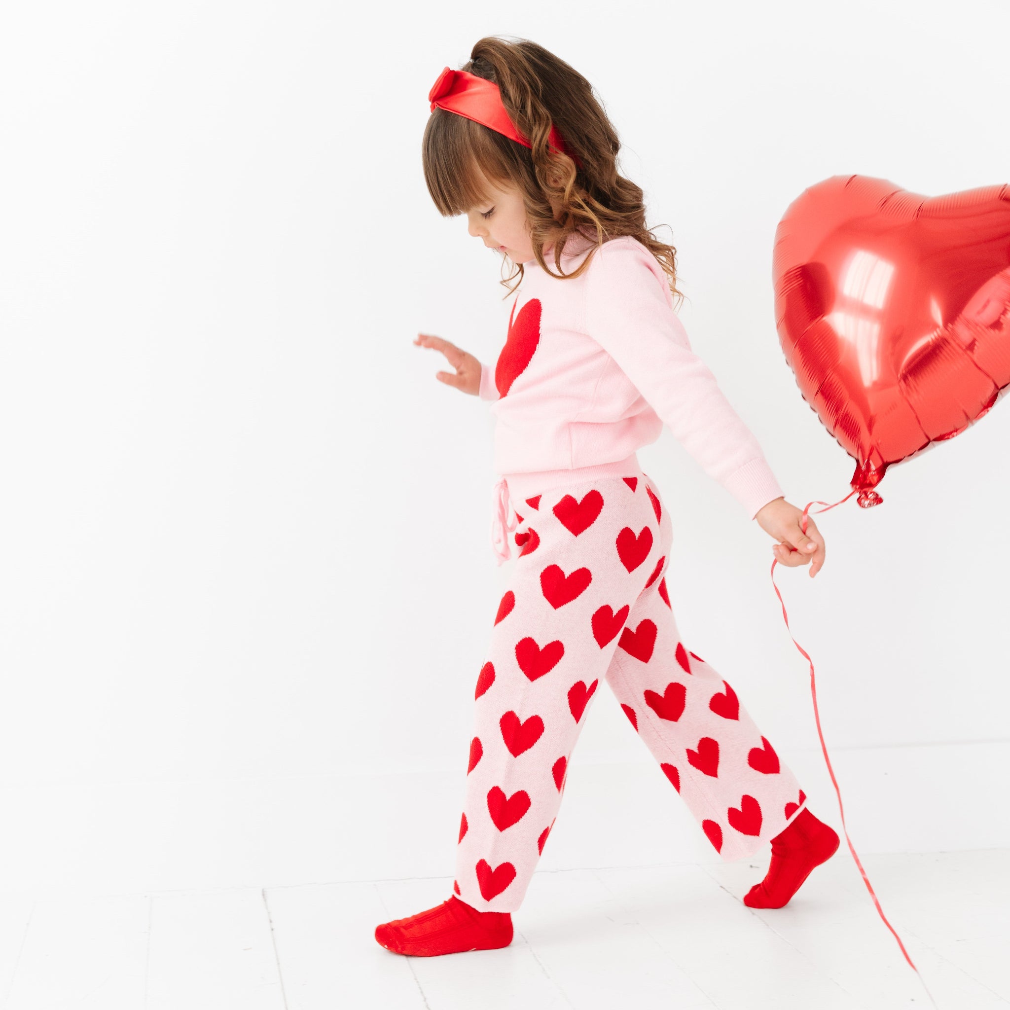 little girl holding heart balloon in pink and red heart sweater set and matching red satin headband