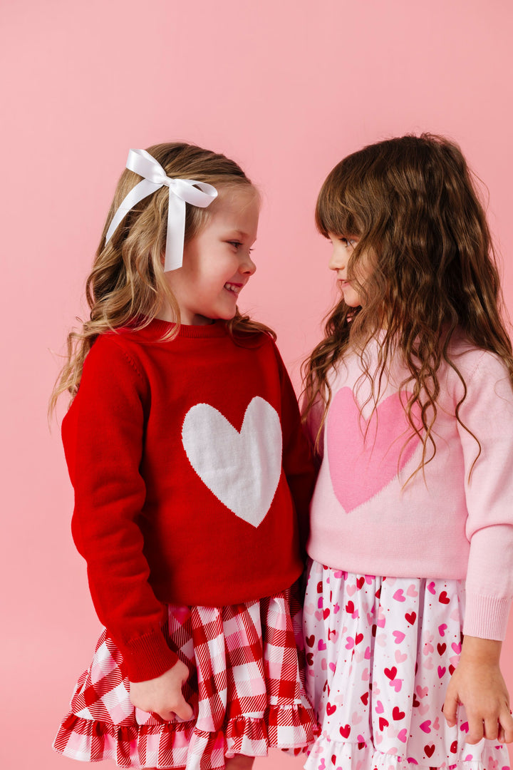 two girls wearing heart sweaters in classic red and white and pastel pink paired with matching valentine's print twirl dresses