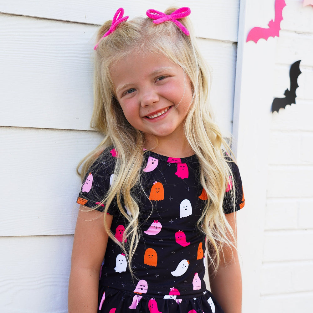 little girl in matching black with colorful ghost print top and skort paired with pink yarn pigtail bows
