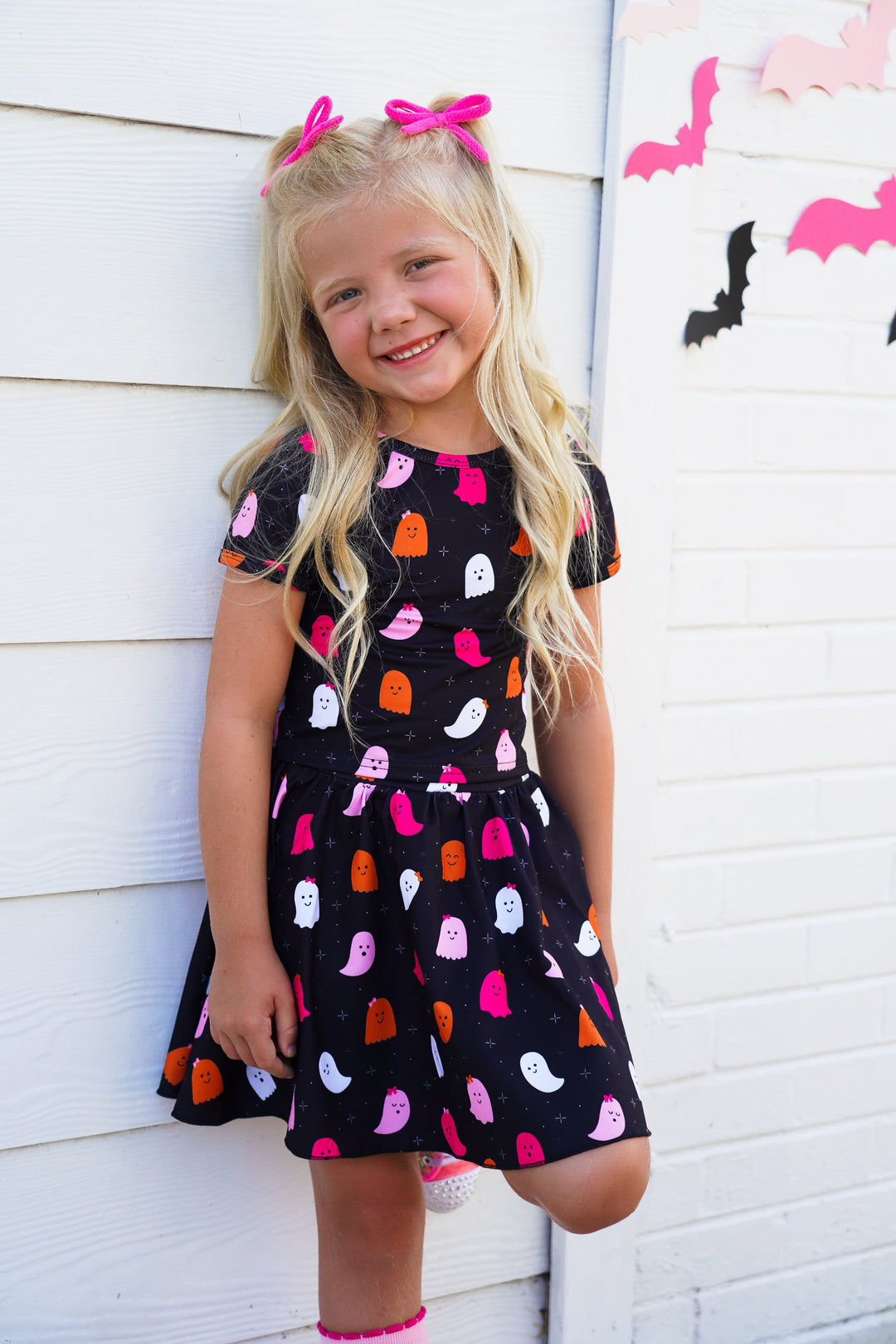 little girl in matching black with colorful ghost print top and skort paired with pink yarn pigtail bows