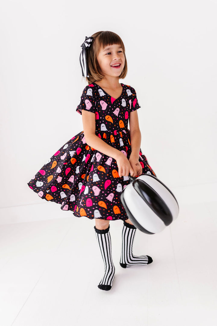 little girl twirling in ghost print halloween dress with matching black and white stripe knee highs and hair bow