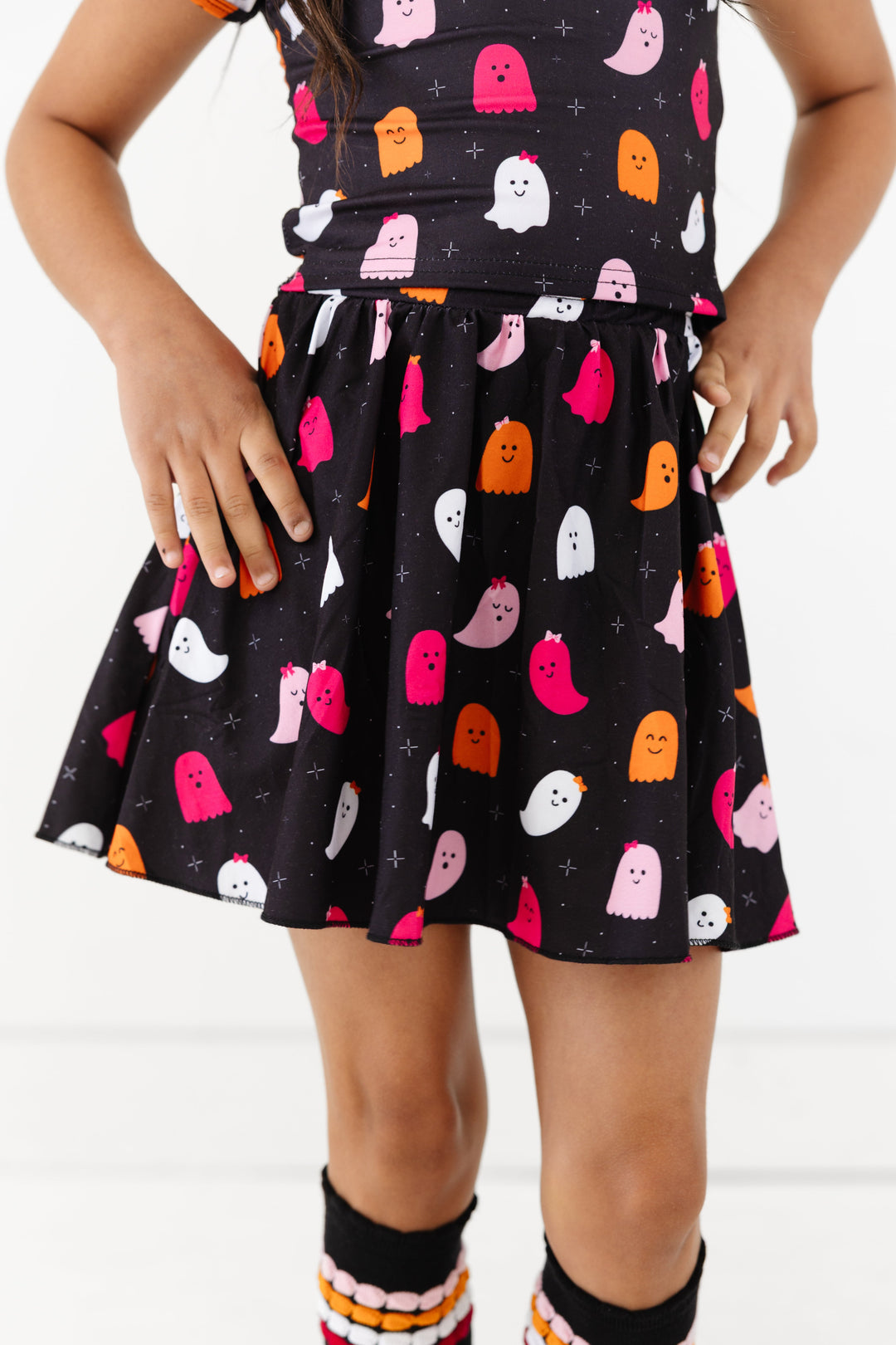 little girl in printed black skort with ghosts wearing little bows and matching top for Halloween