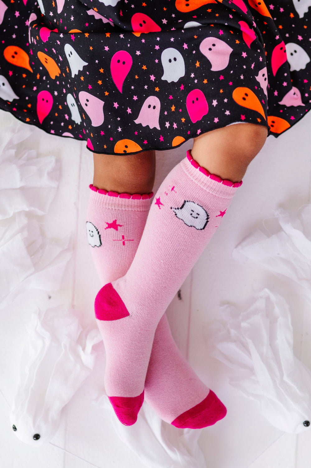 young girl sitting in black lettuce trim twirl dress with colorful ghost print paired with two-tone pink knee socks with ghost and star design