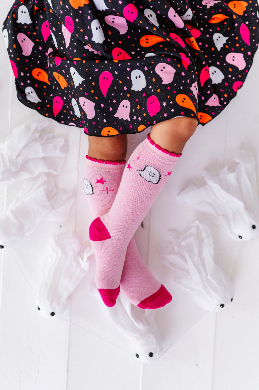 young girl sitting in black lettuce trim twirl dress with colorful ghost print paired with two-tone pink knee socks with ghost and star design