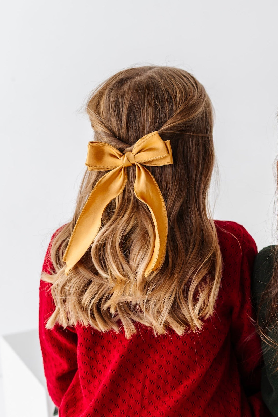 girl sitting backward wearing gold satin hair bow with double bow top, long tails photographed on a white background