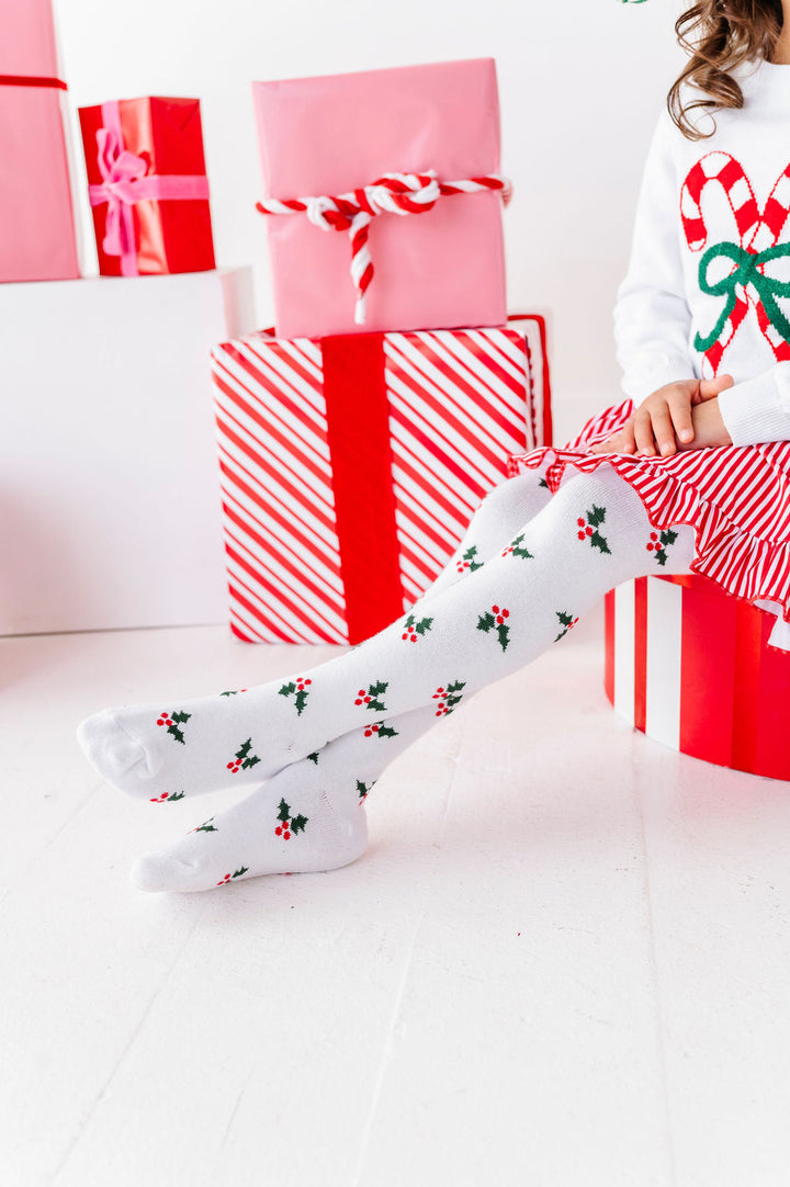 girl sitting with christmas gifts wearing holly cotton tights with matching christmas dress and sweater