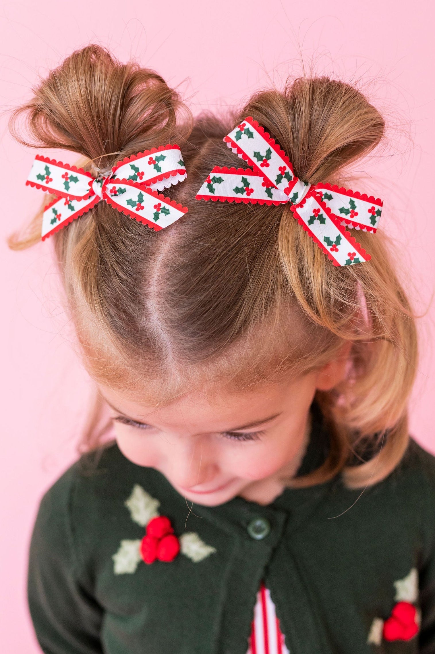 little girl with pigtail buns and holly printed scallop ribbon pigtail bows and knit holly cardigan sweater