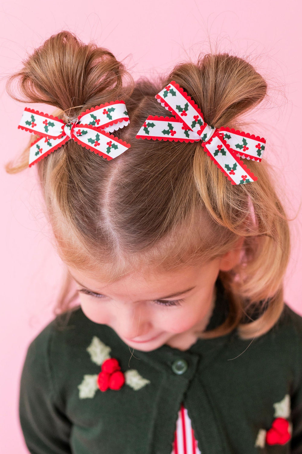 little girl with pigtail buns and holly printed scallop ribbon pigtail bows and knit holly cardigan sweater