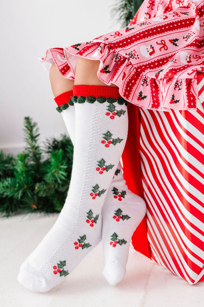 little girl sitting on christmas present wearing holly knee high socks with matching christmas dress