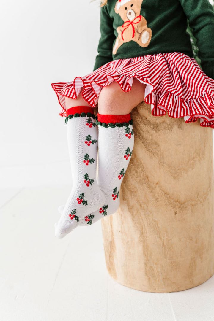 little girl wearing christmas outfit with holly knee high socks